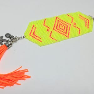 May include: A neon yellow beaded bracelet with a geometric pattern in red. The bracelet features a silver charm with a starfish and an orange tassel. It also has a silver charm with two neon green and orange beads.