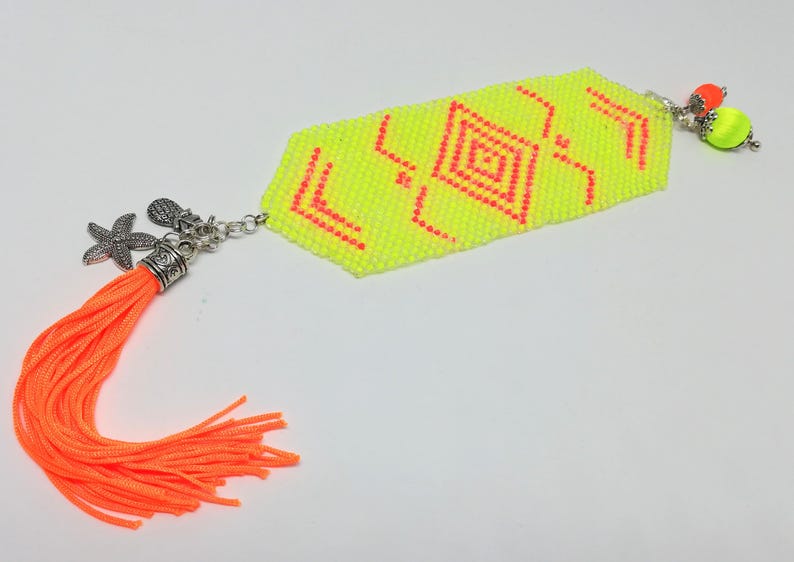 May include: A neon yellow beaded bracelet with a geometric pattern in red. The bracelet features a silver charm with a starfish and an orange tassel. It also has a silver charm with two neon green and orange beads.