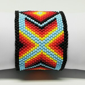 May include: A wide beaded bracelet with a colorful geometric pattern. The bracelet features a black border and a central design in red, orange, yellow, and light blue. The bracelet is displayed on a white surface.