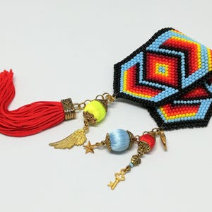 May include: A beaded bracelet with a geometric pattern in red, orange, yellow, and blue. It features a red tassel and decorative charms, including a wing, star, and key, with yellow and blue accents.