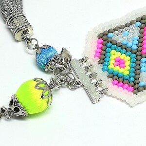 May include: Close-up of a colorful beaded bracelet with a silver clasp and tassel. The bracelet features a geometric pattern in pink, blue, yellow, and gray beads. The tassel and decorative beads are in bright colors.