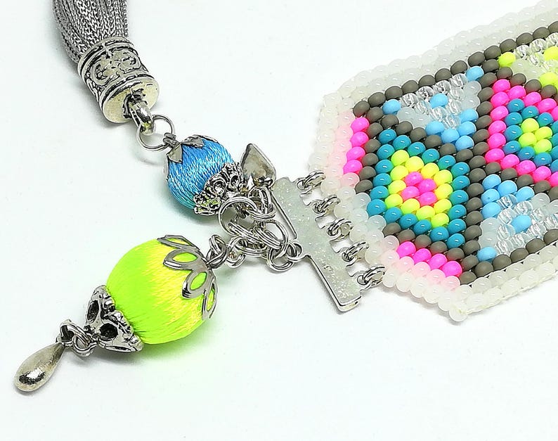 May include: Close-up of a colorful beaded bracelet with a silver clasp and tassel. The bracelet features a geometric pattern in pink, blue, yellow, and gray beads. The tassel and decorative beads are in bright colors.