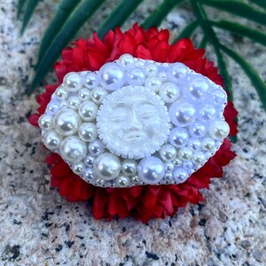 May include: A white pearl and face cameo brooch with a red flower background.