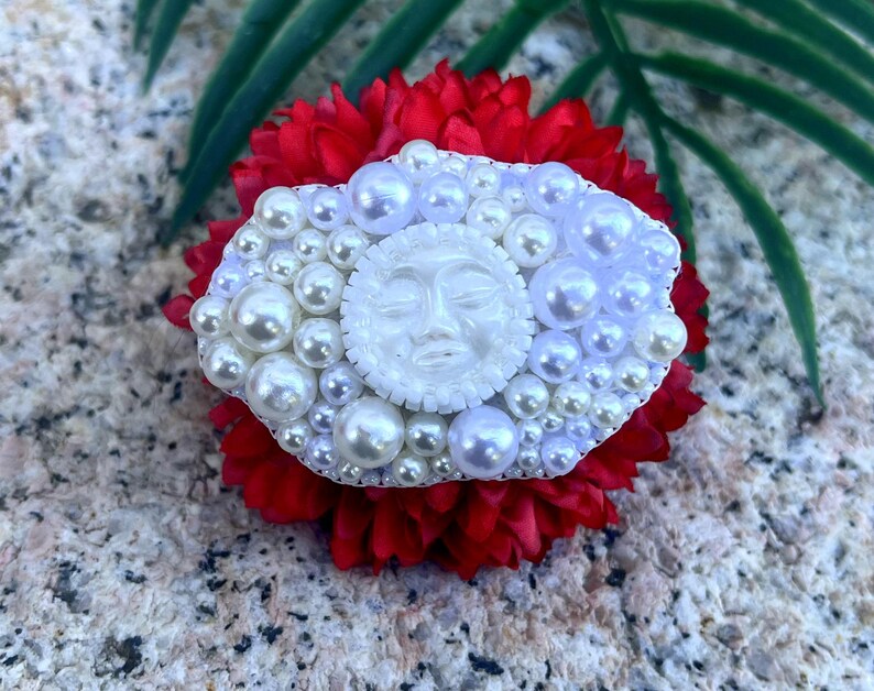 May include: A white pearl and face cameo brooch with a red flower background.