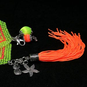May include: A beaded bracelet in neon green and orange, with silver pineapple and starfish charms. An orange tassel and a small beaded ball with orange and green accents are also attached.