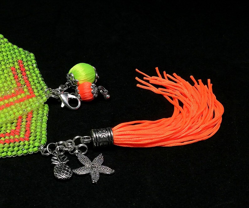 May include: A beaded bracelet in neon green and orange, with silver pineapple and starfish charms. An orange tassel and a small beaded ball with orange and green accents are also attached.