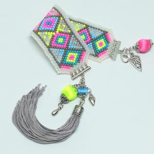 May include: A colorful beaded bracelet with a geometric pattern in neon pink, yellow, blue, and gray. The bracelet has silver-tone clasps and charms, including a tassel and a pink silk-wrapped bead. The bracelet is a unique fashion accessory.