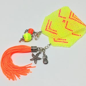 May include: A neon yellow beaded accessory with orange detailing. Features an orange tassel, silver charms of a starfish and pineapple, and a beaded geometric design. Includes a chain and two small beaded spheres.