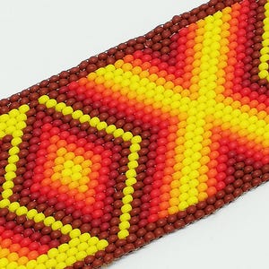 Op de afbeelding: Close-up van een kralenarmband met een levendig, geometrisch patroon. Het ontwerp heeft een kleurengradient van geel, oranje en rood, met een donkerbruine rand. De kralen zijn klein en strak geweven, waardoor een textuur ontstaat.