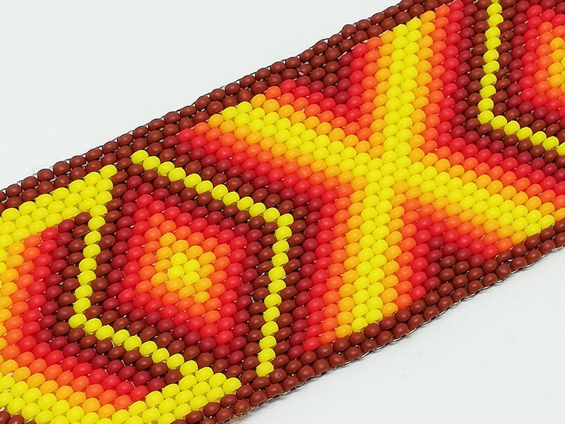 Op de afbeelding: Close-up van een kralenarmband met een levendig, geometrisch patroon. Het ontwerp heeft een kleurengradient van geel, oranje en rood, met een donkerbruine rand. De kralen zijn klein en strak geweven, waardoor een textuur ontstaat.