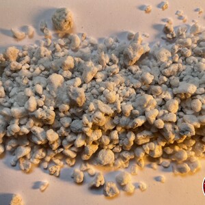 May include: A collection of small, irregular, off-white, porous, and textured mineral-like granules scattered across a surface. The pieces vary in size and shape, exhibiting a rough, uneven surface structure. A circular logo with the text THE BENDER is visible.