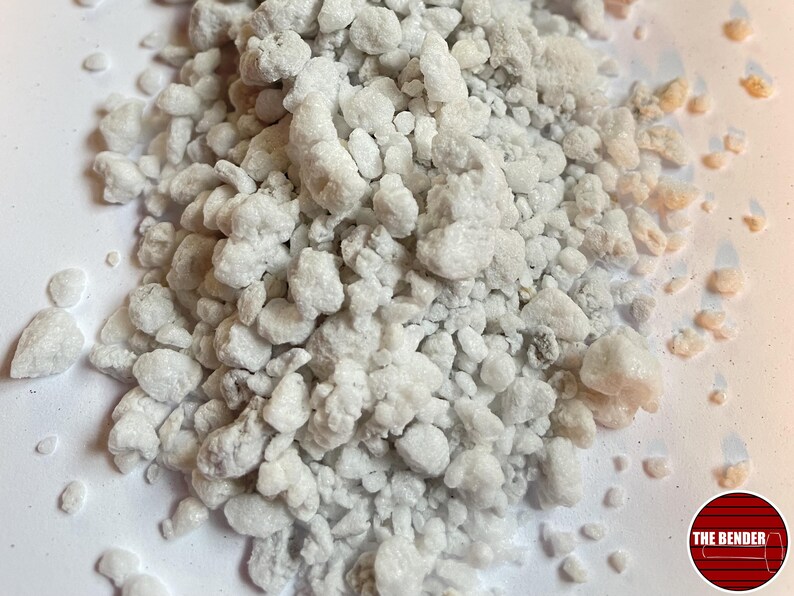 May include: A pile of white, porous, irregular perlite granules with a rough, rocky texture. In the bottom right corner, there is a circular red logo containing horizontal black lines and the white text THE BENDER.