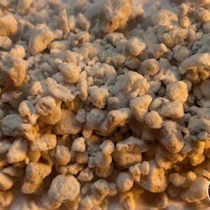 May include: A collection of small, irregular, off-white granular particles with a porous, rocky texture. The pieces vary in size and shape, creating a dense, uneven surface. A circular red logo with white horizontal lines and the text THE BENDER is visible.