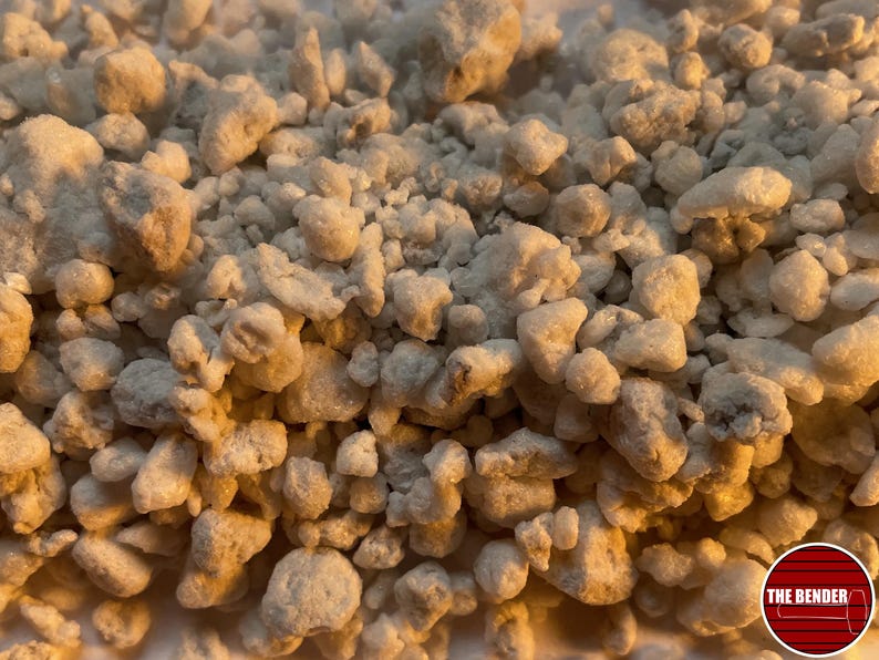 May include: A collection of small, irregular, off-white granular particles with a porous, rocky texture. The pieces vary in size and shape, creating a dense, uneven surface. A circular red logo with white horizontal lines and the text THE BENDER is visible.