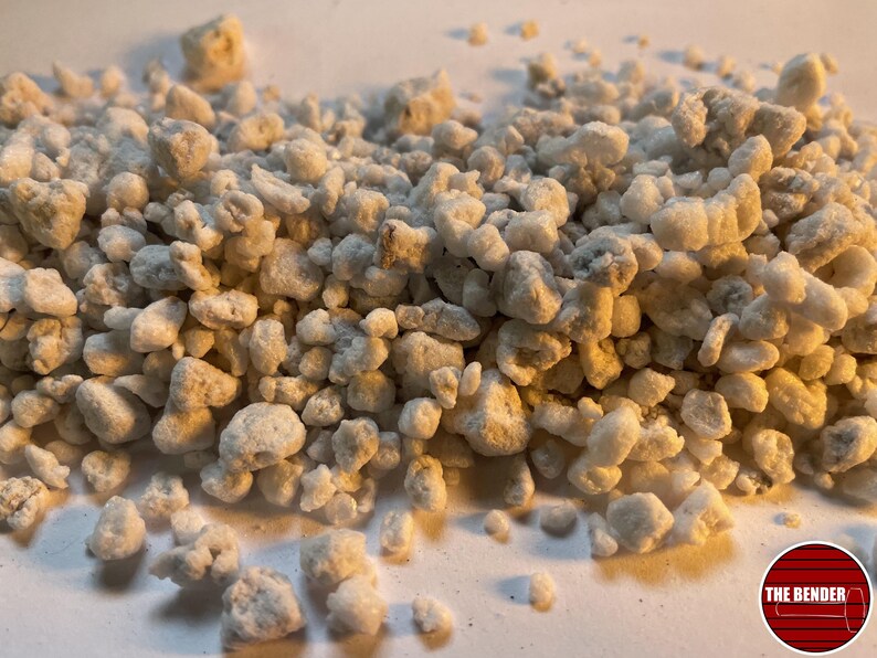 May include: A collection of small, irregular, off-white perlite granules with a porous, lightweight texture. The particles vary in size and shape, displaying a matte finish. A circular logo in the bottom right corner features the text THE BENDER.