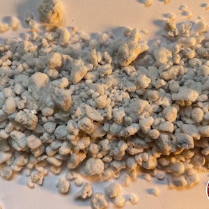 May include: A collection of small, irregular, off-white, and textured granular pieces scattered across a surface. In the bottom right corner, there is a circular red logo containing horizontal lines and the white text THE BENDER.