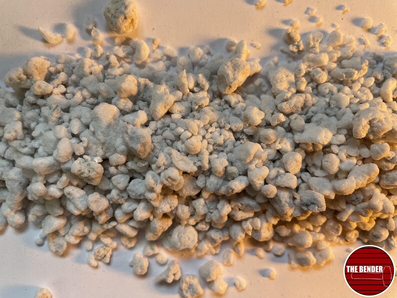 May include: A collection of small, irregular, off-white, and textured granular pieces scattered across a surface. In the bottom right corner, there is a circular red logo containing horizontal lines and the white text THE BENDER.