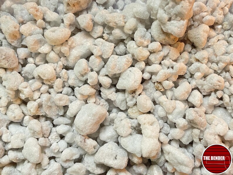 May include: A collection of small, irregular, off-white and light gray porous mineral stones with a rough, textured surface. The stones vary in size and shape, creating a dense, uneven layer. A circular red logo with the text THE BENDER is visible.
