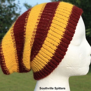 May include: A slouchy beanie hat with yellow and maroon stripes. The hat is made of knitted fabric and is worn on a white mannequin head.