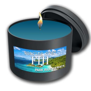 May include: A black candle jar with a blue wax interior and a lid. The jar has a label that reads "soaring over FIJI PARK RIDE SERIES" and features a tropical island scene.
