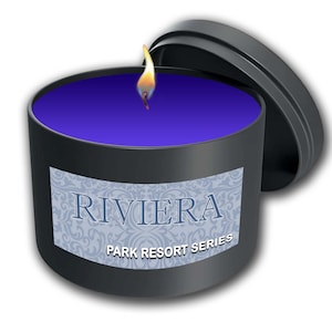 May include: A lit, black candle in a round tin with a lid. The candle has a deep purple wax and a label that reads "RIVIERA PARK RESORT SERIES" in blue text. The flame is yellow and orange.