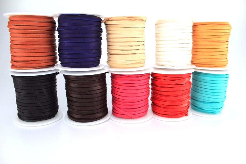 K&ouml;nnte beinhalten: Zehn Spulen mit Lederkordel in verschiedenen Farben, darunter Orange, Lila, Beige, Wei&szlig;, Braun, Schwarz, Pink, Rot, T&uuml;rkis und Braun. Die Spulen sind in einer Reihe auf einer wei&szlig;en Oberfl&auml;che angeordnet.