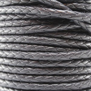 May include: Close-up of a spool of black braided leather cord. The cord is tightly wound and has a smooth, polished finish.