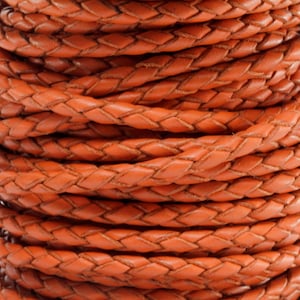May include: A close-up of a spool of braided leather cord. The cord is a rich orange-brown color and has a smooth, polished finish.