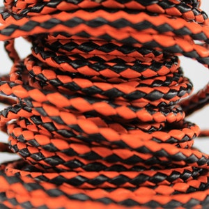 May include: Close-up of a spool of black and orange braided leather cord. The cord is tightly wound and has a textured surface.