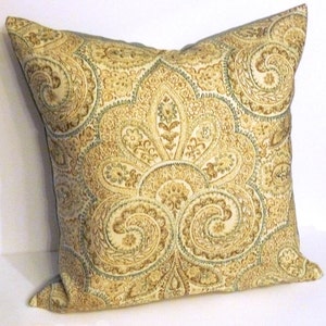 May include: Decorative square pillow with a detailed paisley pattern in shades of gold, brown, and teal. The pillow has a soft, textured appearance and a classic design, suitable for home decor.