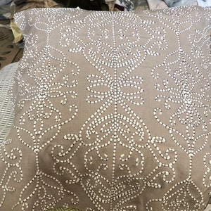 Peut inclure: Un coussin beige avec un motif floral brodé blanc. Le coussin est fait d'un tissu doux et texturé.