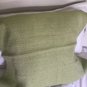 May include: A green and white patterned pillow with a diamond design. The pillow is rectangular and rests on a white surface, likely a bed. The pillowcase has a woven texture.