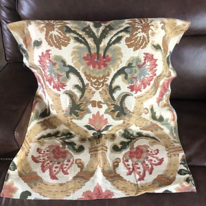 Puede incluir: Una almohada decorativa con un patrón floral en tonos marrones, rosas y verdes. La almohada tiene un fondo blanco y un diseño tipo damasco.