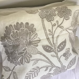 May include: A white pillow with a floral pattern embroidered in gray. The flowers are stylized and have a vintage look.