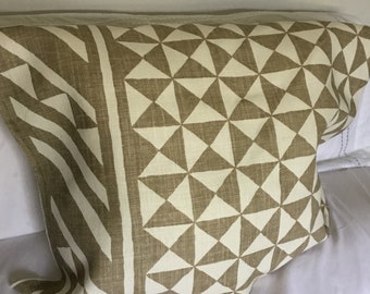 May include: A decorative pillow with a geometric pattern. The pillow features a repeating design of triangles in a light beige color against a darker beige background. The pillow has a striped border on one side.