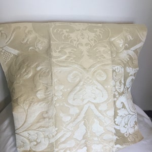 May include: A cream-colored fabric with a white damask pattern. The fabric has a subtle sheen and a soft texture.
