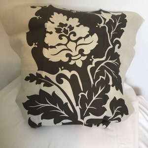 May include: A white pillow with a brown floral pattern. The pattern features large leaves and a stylized flower.