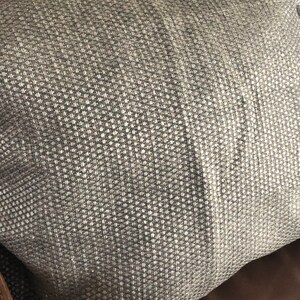 Puede incluir: Una almohada gris de tejido tejido texturizado. La almohada está hecha de un material suave y cómodo y tiene un brillo sutil.
