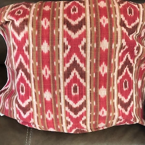 Könnte beinhalten: Rotes, braunes und weißes Kissen mit einem Ikat-Muster.