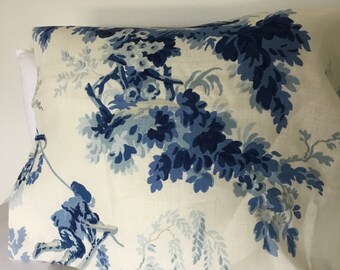 May include: A white pillowcase with a blue floral pattern. The pattern features blue flowers, leaves, and branches. There are also two small blue figures in the pattern.