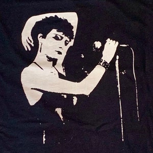 May include: Black and white image of a person singing into a microphone. The person is wearing a dark dress and has short, dark hair.