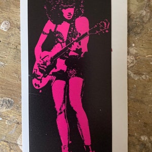 May include: A black and white image of a person playing a guitar. The person is wearing a pink outfit and has a large afro. The guitar is a light brown color.