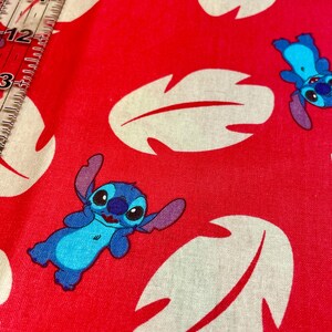 May include: Red fabric with a repeating pattern of white leaf shapes and blue cartoon character Stitch. Ideal for crafting, the fabric could be used for clothing or home decor projects.