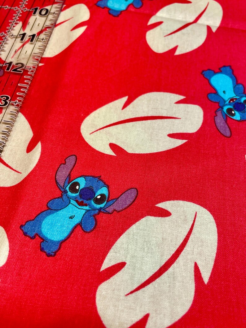 May include: Red fabric with a repeating pattern of white leaf shapes and blue cartoon character Stitch. Ideal for crafting, the fabric could be used for clothing or home decor projects.