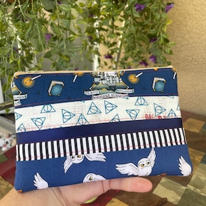 May include: A rectangular, multi-fabric pouch with a zipper closure. The design features blue fabric with white owls, a white fabric with geometric shapes, and a blue fabric with text and illustrations. A wand is visible in the foreground.