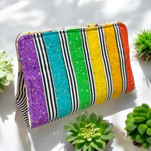 May include: A rainbow striped fabric pouch with a white background and black stripes. The pouch is quilted and has a zipper closure.