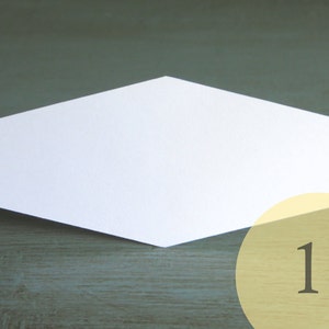 May include: A white, hexagonal-shaped card with a 1-inch measurement label. The card is on a dark green wooden surface.