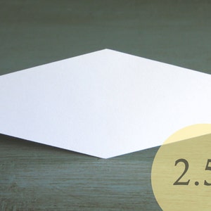 May include: A white, hexagonal place card with a 2.5 inch measurement printed on it. The place card is sitting on a dark green wooden surface.