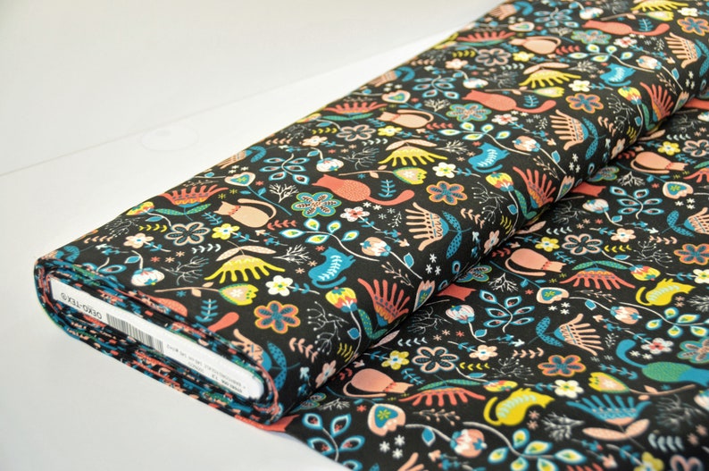 May include: Black fabric with a repeating pattern of colorful cats, flowers, and leaves. The fabric is rolled up and the label is visible.
