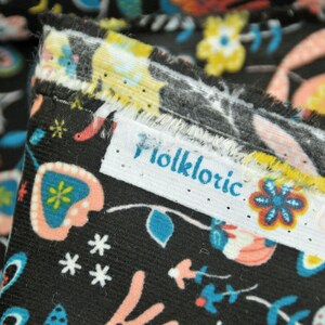 May include: Close-up of black fabric with a colorful floral pattern. The fabric has a white label with the word "Folkloric" printed on it.